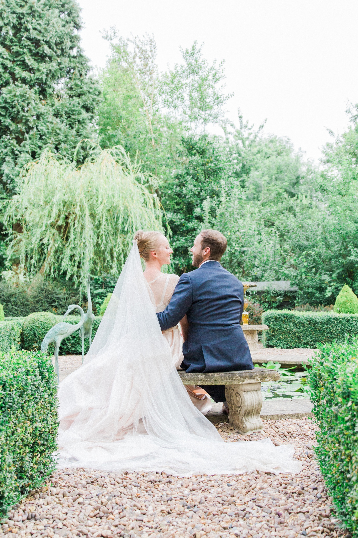 Bride and groom sit on a bench together during their English garden wedding