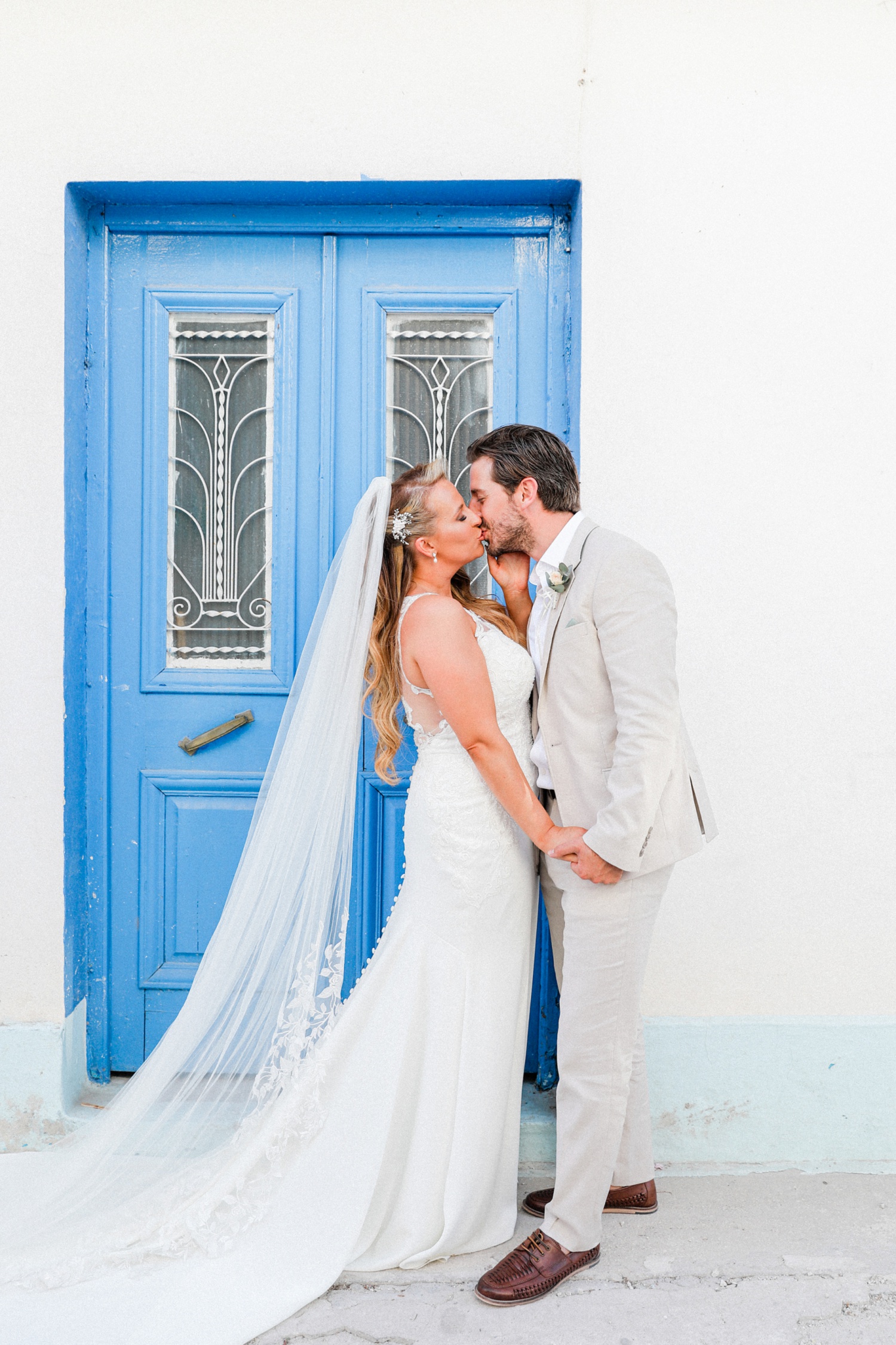 Bride and groom kiss in front of a blue door during their wedding in Parga
