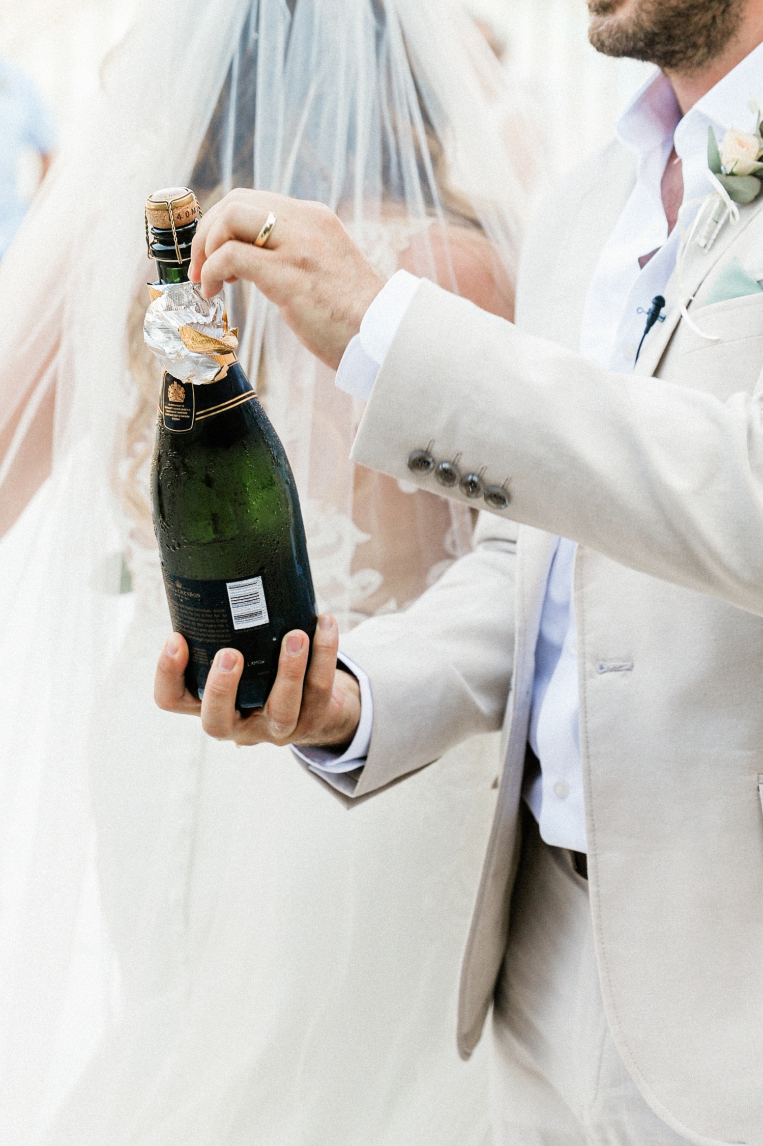 Groom opening a bottle of champagne after his beach wedding