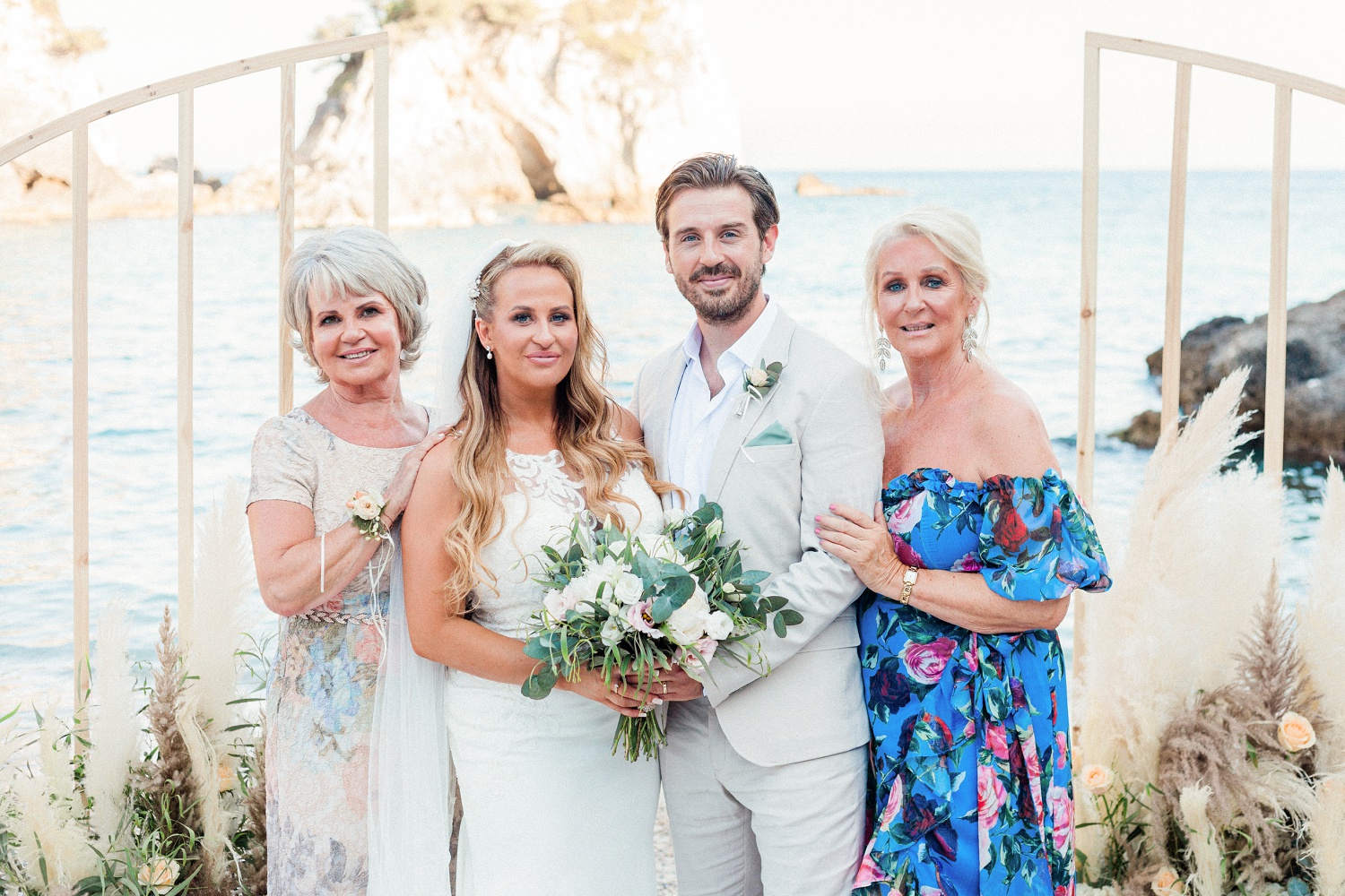 Bride and groom stand with their mothers at a beach wedding in Parga