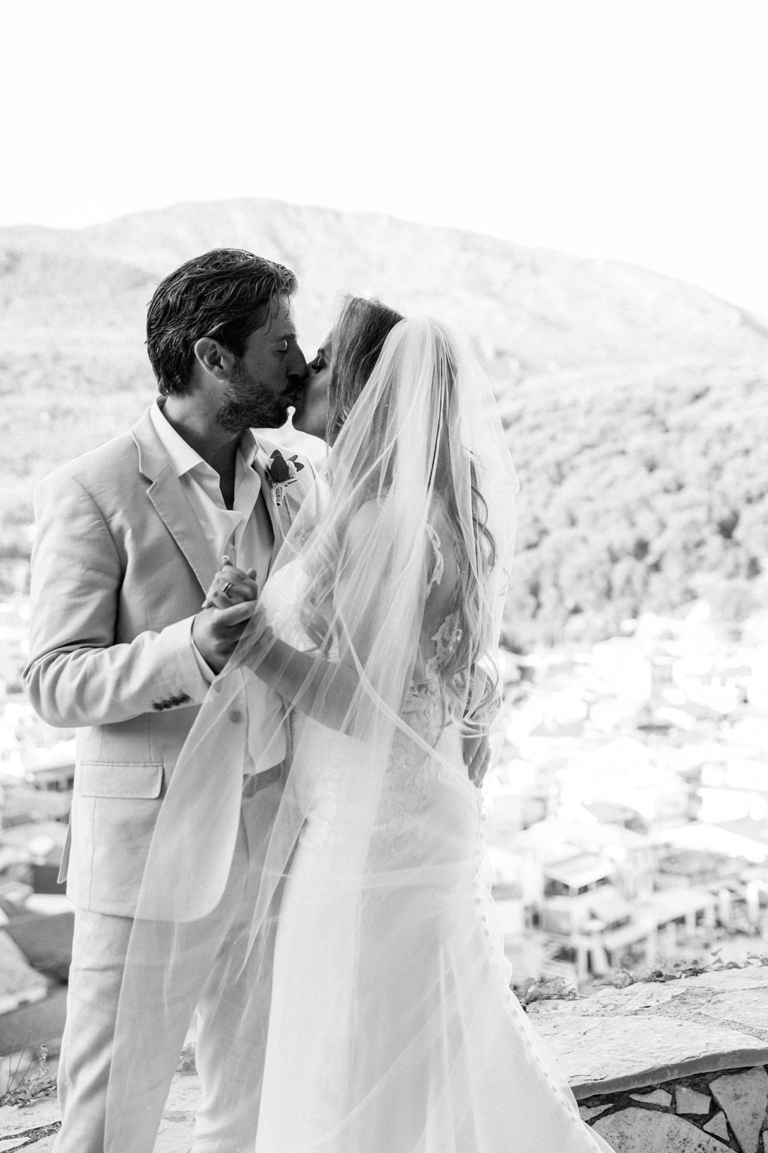 Bride and groom kiss on a terrace with a view of Parga harbour below