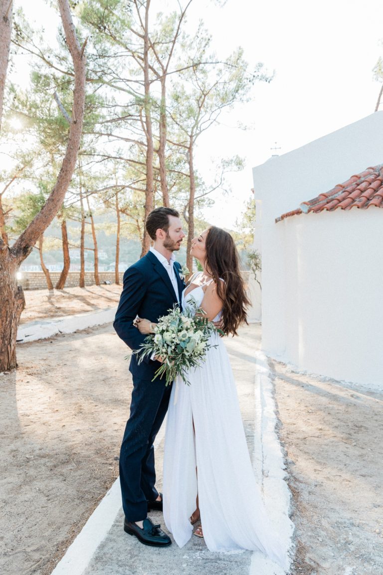 Bride and groom standing on Lazaretto Islet in Ithaca with the white church behind them