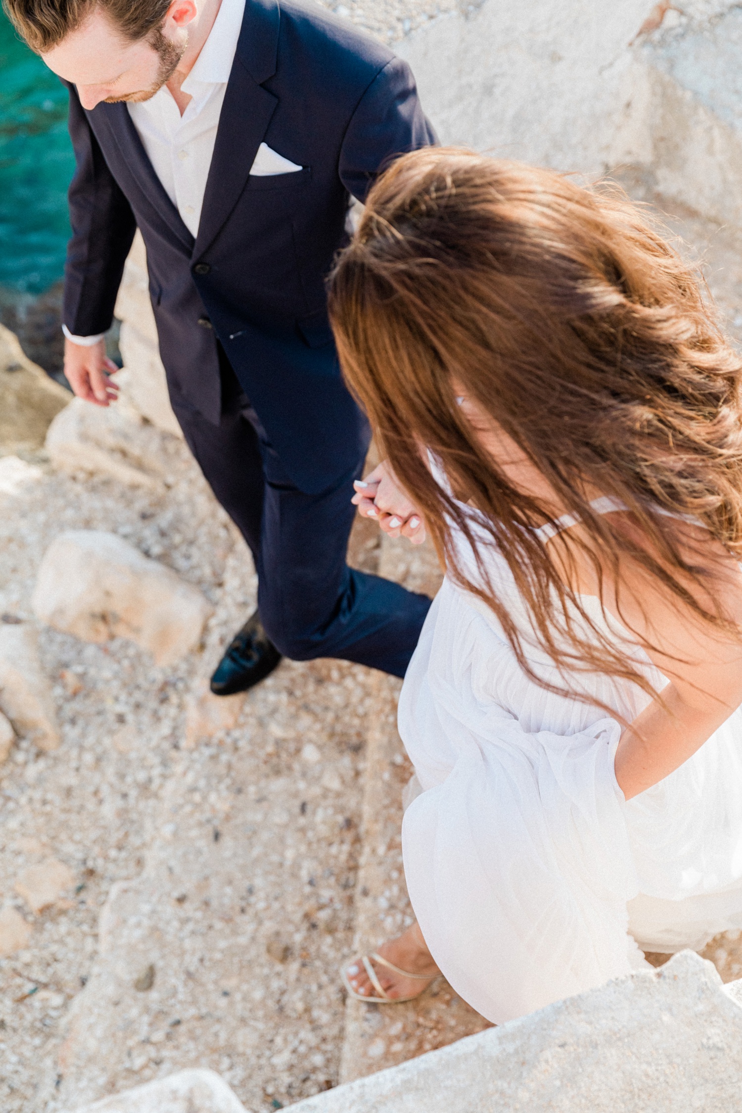 Couple walk down rough stairs to the sea on their wedding day