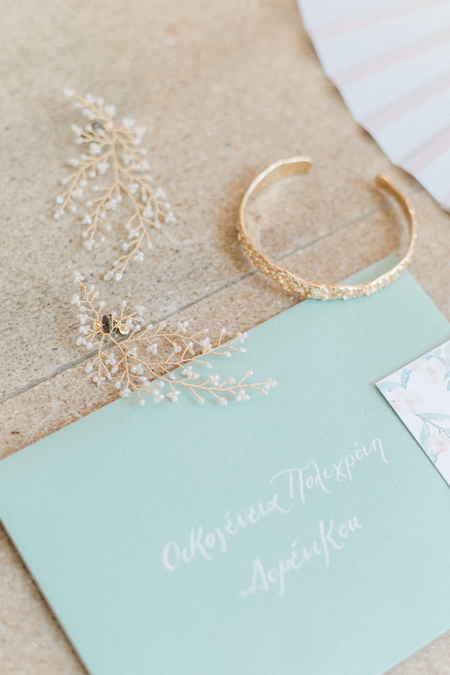 Bridal details including mint envelope with white calligraphy and gold jewellery