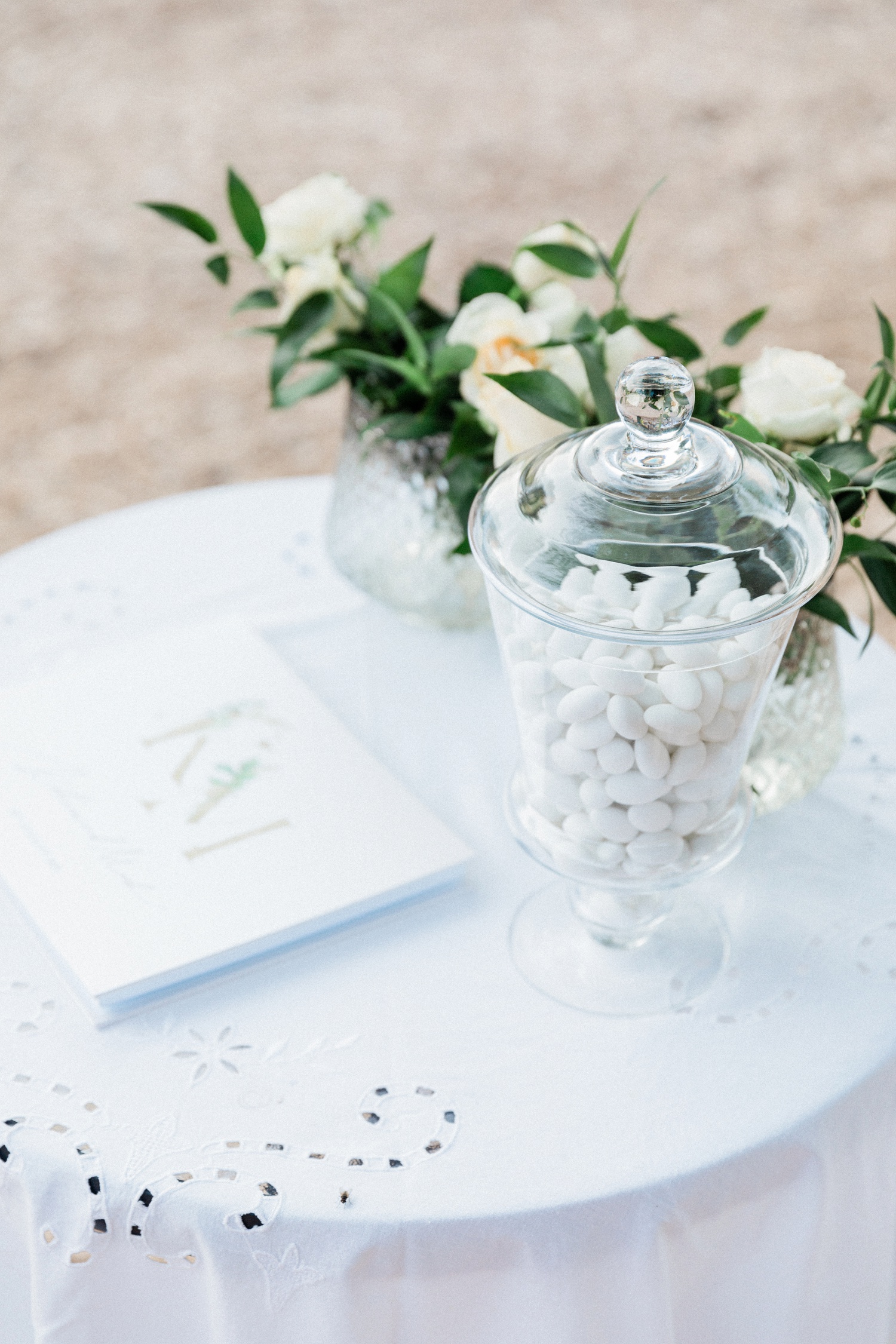 Olive grove wedding welcome table with white candy and rose and greenery arrangements