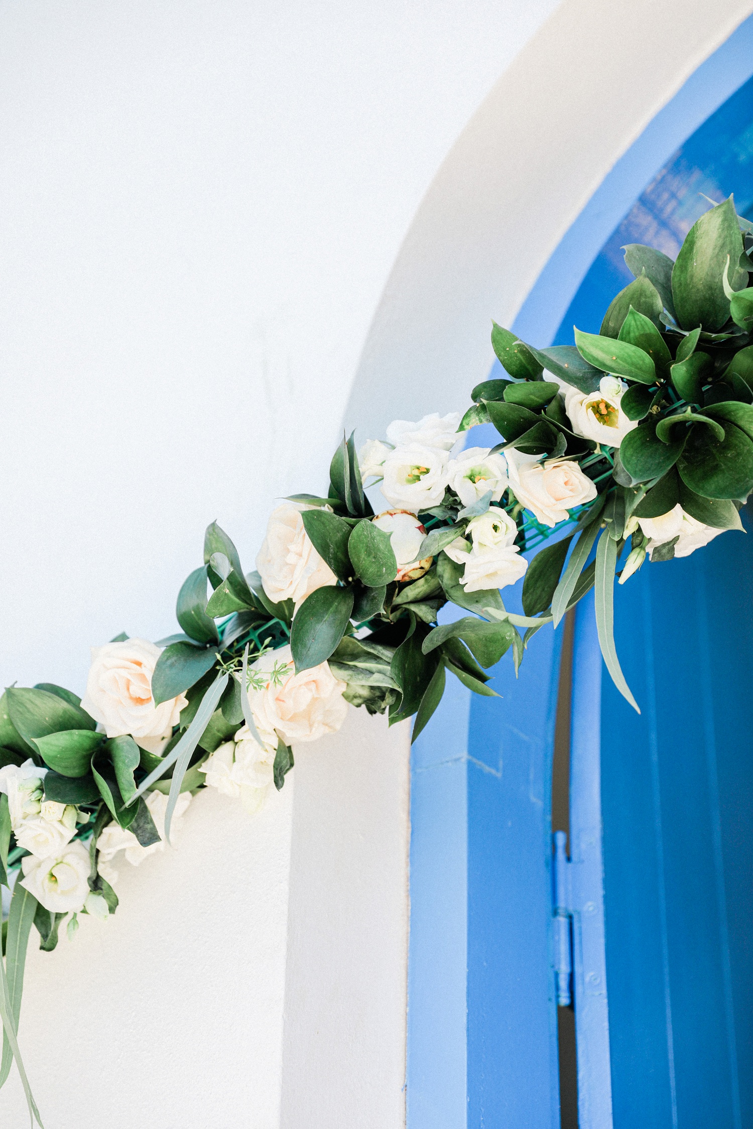 Blue door to a white Greek church decorated with a garland of flowers for a wedding