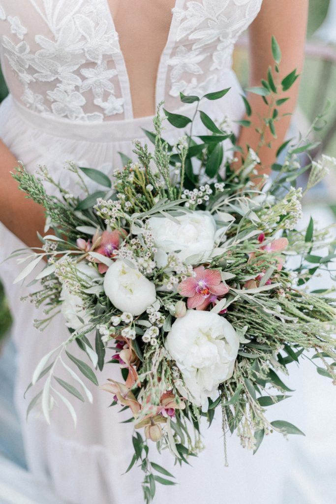 Close up of the bridal bouquet featuring white peonies, ombre pink orchids and olive leaves