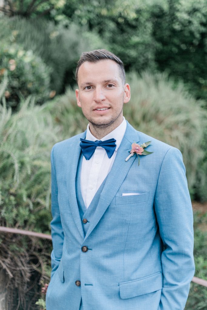 Portrait of the groom wearing a blue suit with a navy bowtie in the gardens of Villa Veneziano